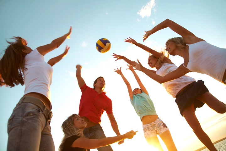 group of young people playing volleyball on the beach